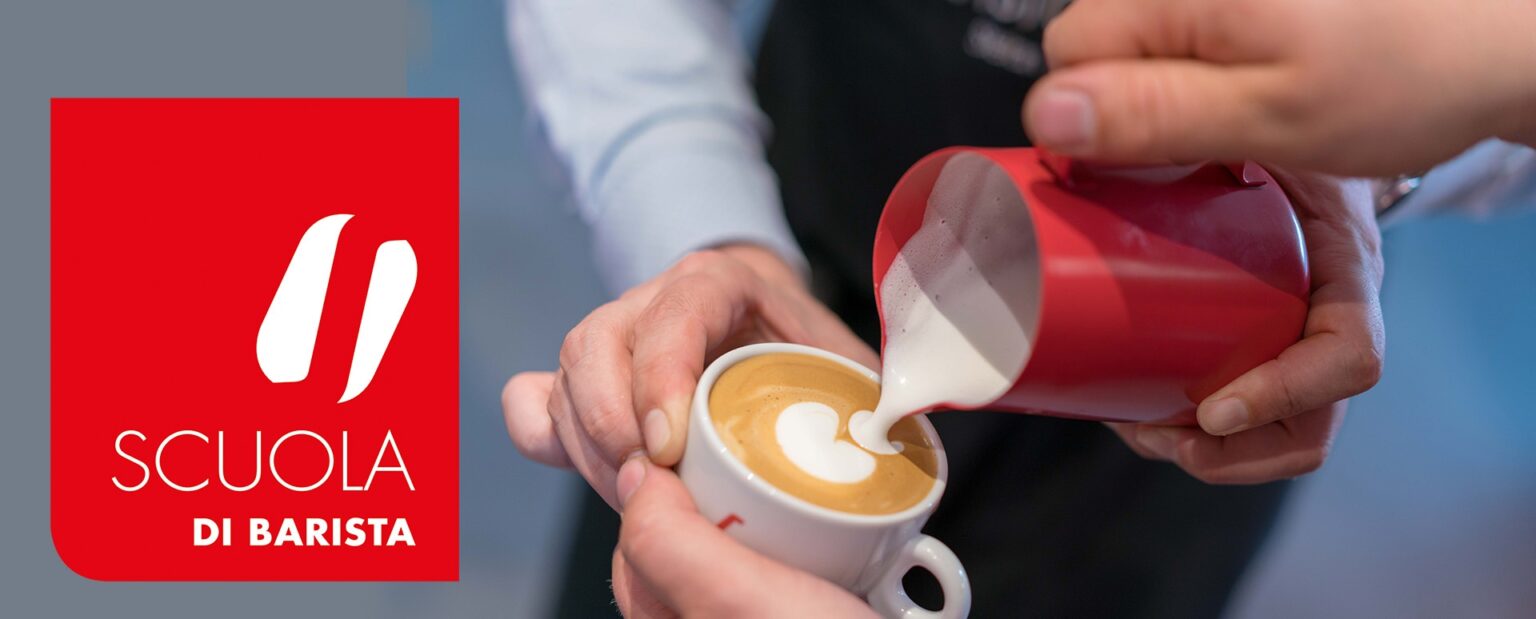 eine Hand schenkt Milch mit Milchschaum in eine Cappuccinotasse die von einer anderen Person gehalten wird