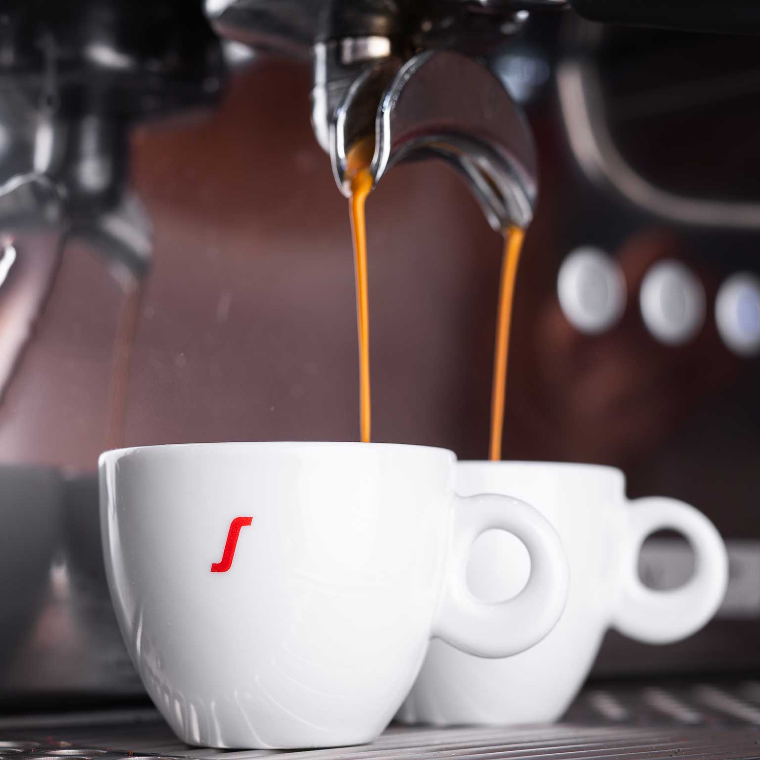 Kaffee fließt aus einem Siebträger in zwei Cappuccinotassen