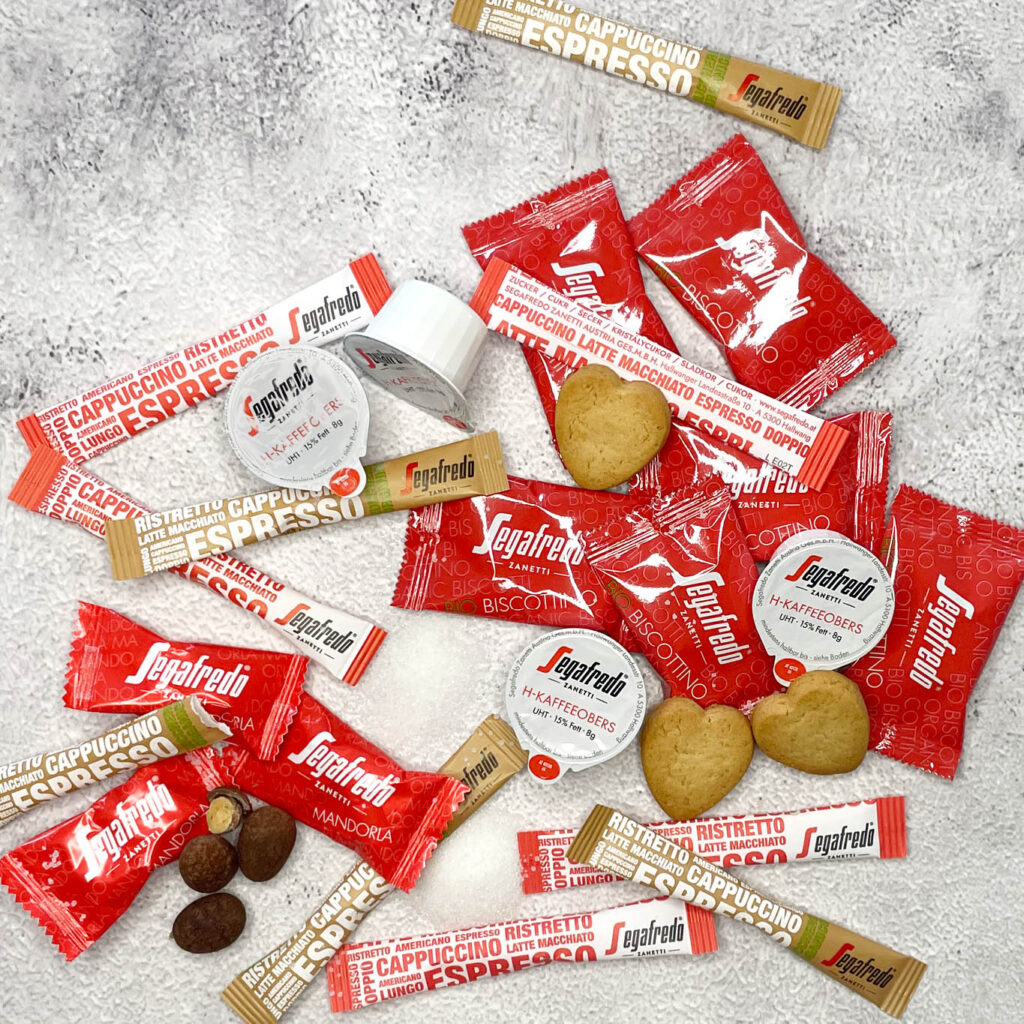 Imagebild Zusatzprodukte mit Zuckersticks, Portionssahne, Schokoladenmandeln und Keksen in Herzform, zum Teil ausgepackt