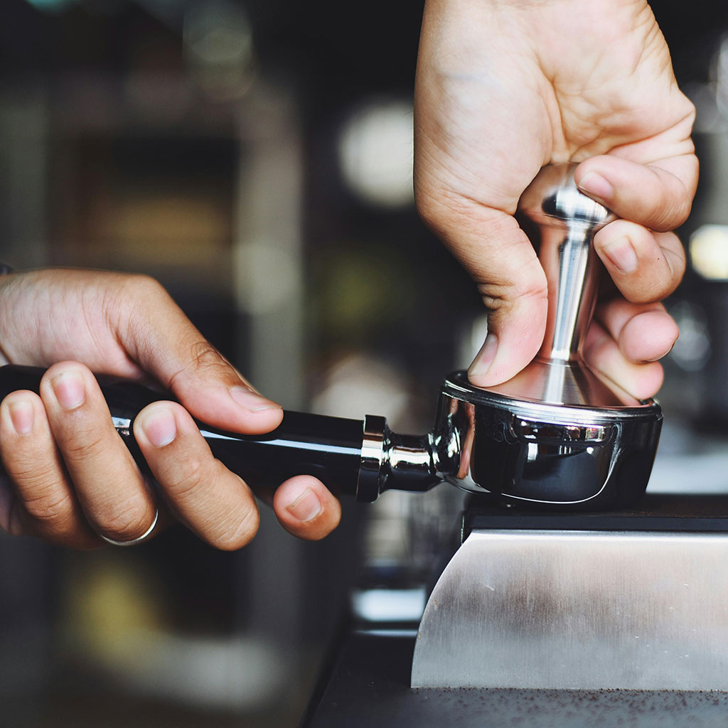 eine Hand tampt Kaffee in einem Siebträger