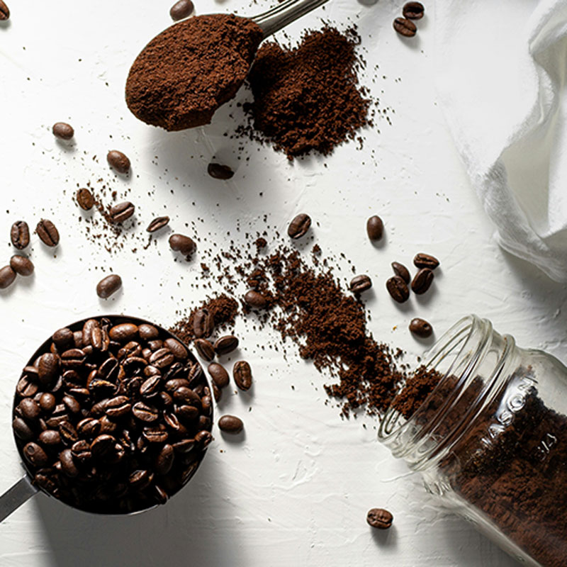 gemahlener Kaffee und Kaffeebohnen sind in Bechern und auf einem Löffel verteilt