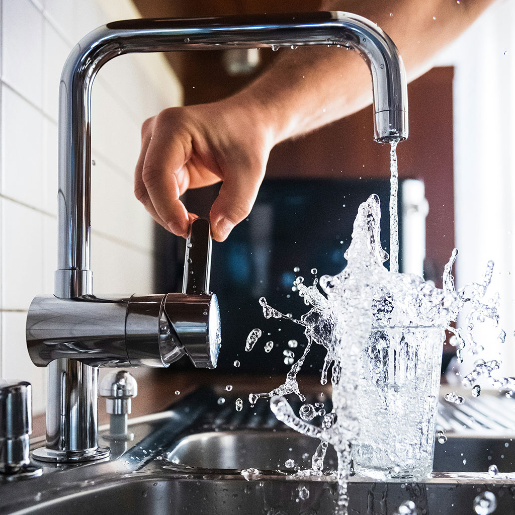 Wasser fließt explosiv aus einem Wasserhahn in ein Glas